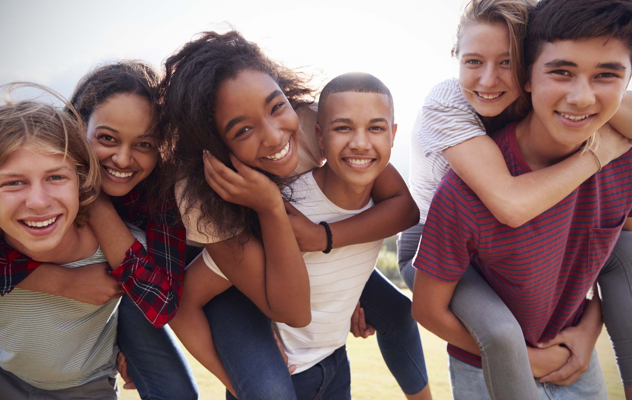 Teenage school friends having fun piggybacking outdoors